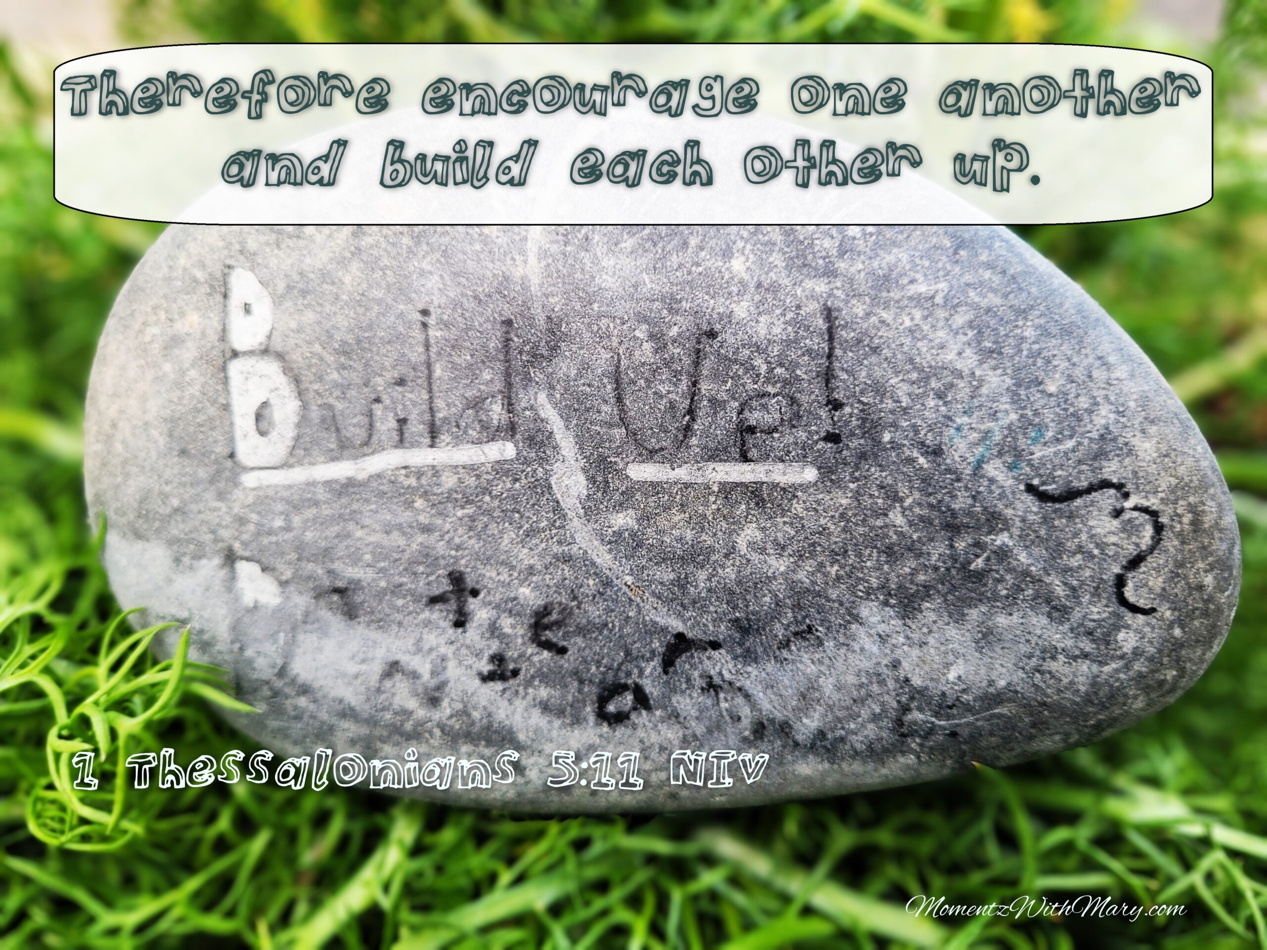 Gray stone on green leaf background. The stone reads Build Up Don't tear down 1 Thessalonians 5:11 New International Version Therefore encourage one another and build each other up