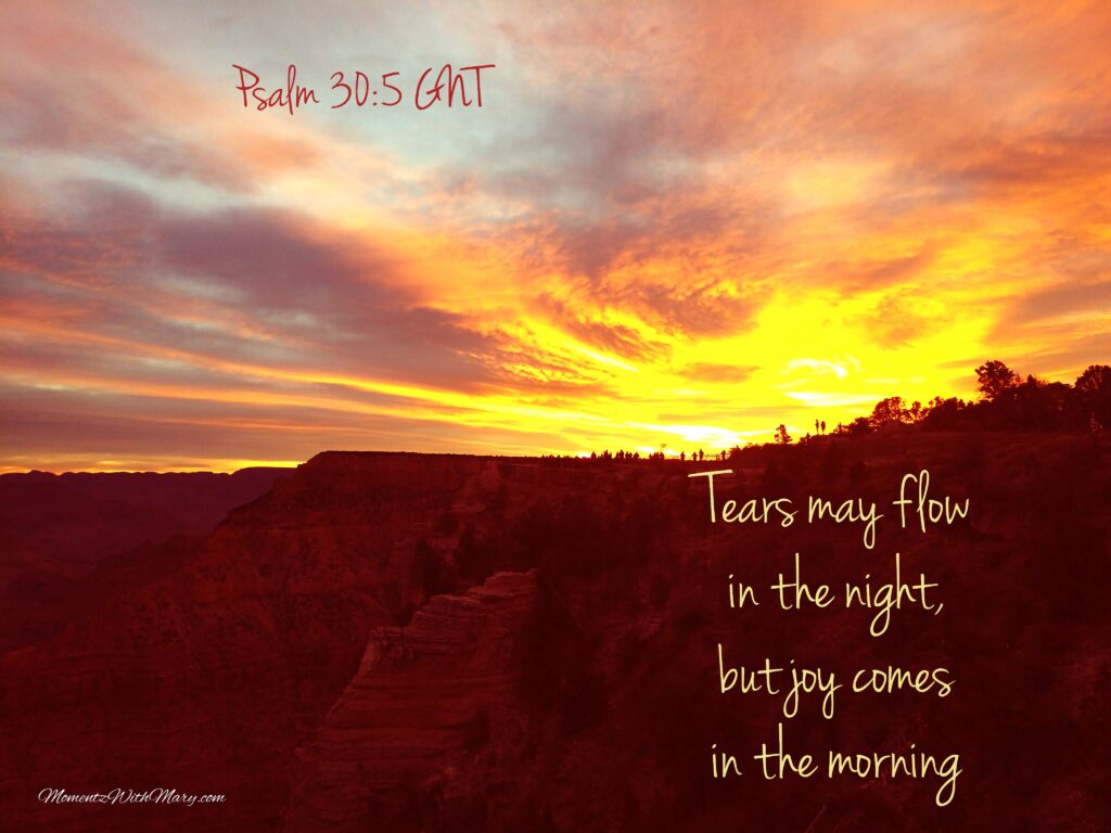 Bright yellow and orange sunrise over the Grand Canyon while people watch in the far distance. Psalm 30:5 Tears may flow in the night, but joy comes in the morning